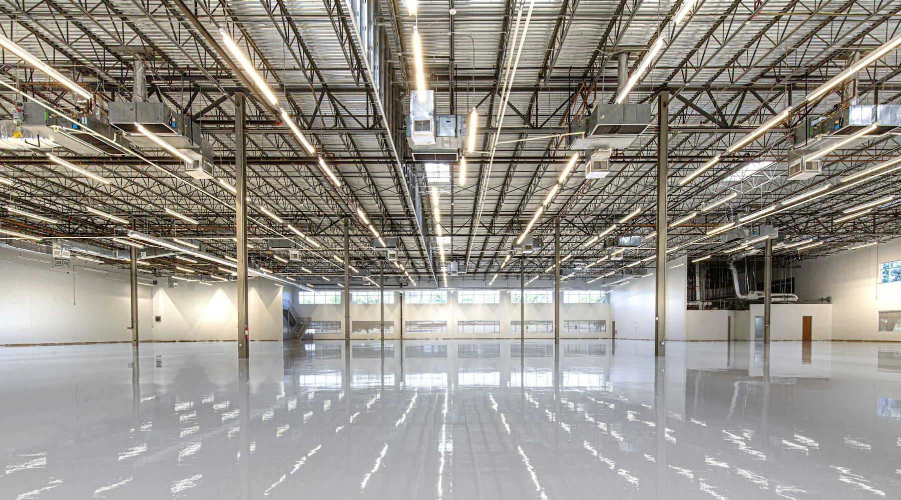 Glossy light-grey epoxy floor in an empty warehouse, reflecting the ceiling lights